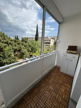 Natkriveni balkon sa drvenim podom i pogledom na zelenilo i okolne zgrade. - image 7