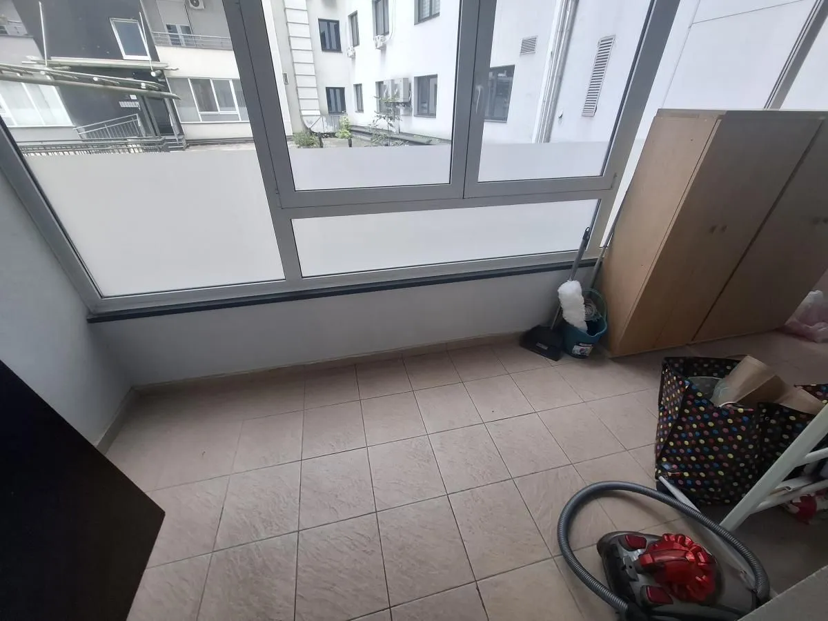 Zastakljeni balkon sa keramičkim pločicama na podu i pogledom na susedne zgrade.