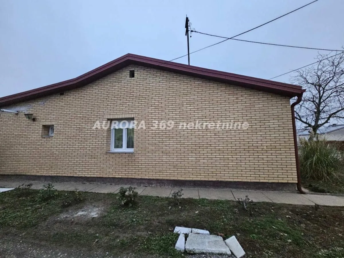 Pogled na fasadu i dvorište prizemne kuće obložene ciglom.