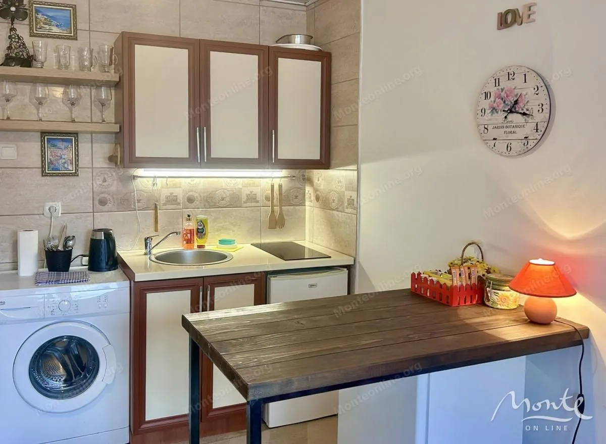 Manja opremljena kuhinja sa sudoperom, ugradnim elementima i trpezarijskim stolom.