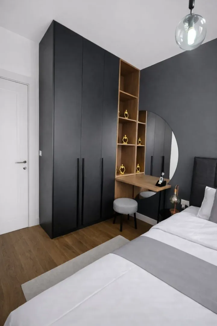 Modern bedroom with a black wardrobe, wooden shelves, and a bed.