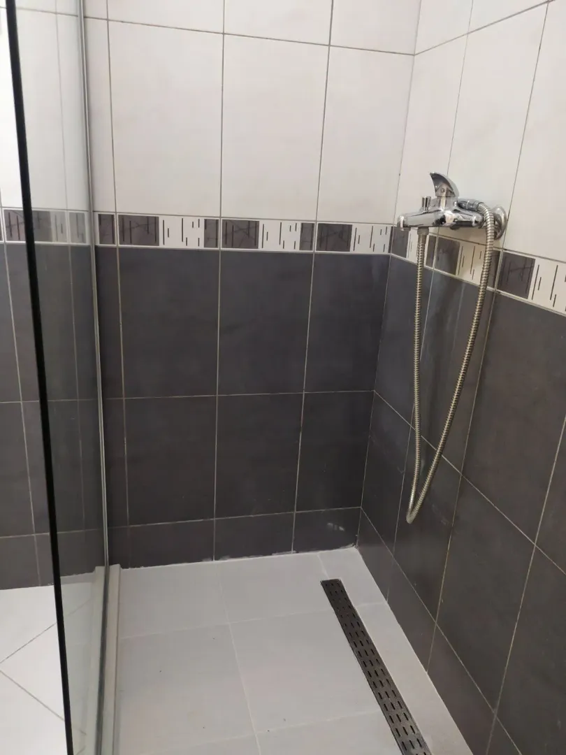 Tuš kabina obložena tamnim i svijetlim pločicama.