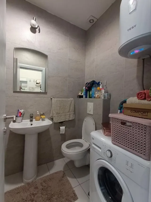 Smaller bathroom with a washbasin, toilet bowl, washing machine and water heater.