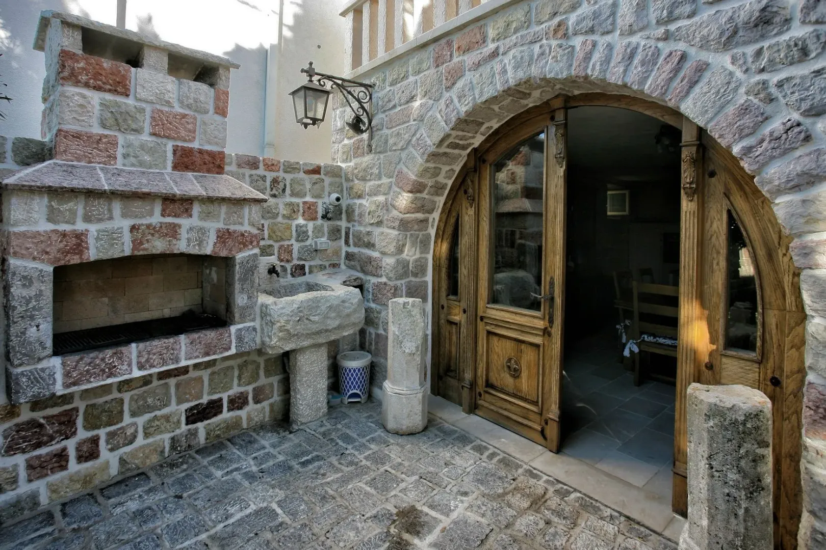 A stone courtyard featuring a built-in barbecue grill, a stone sink, and a large arched wooden door.