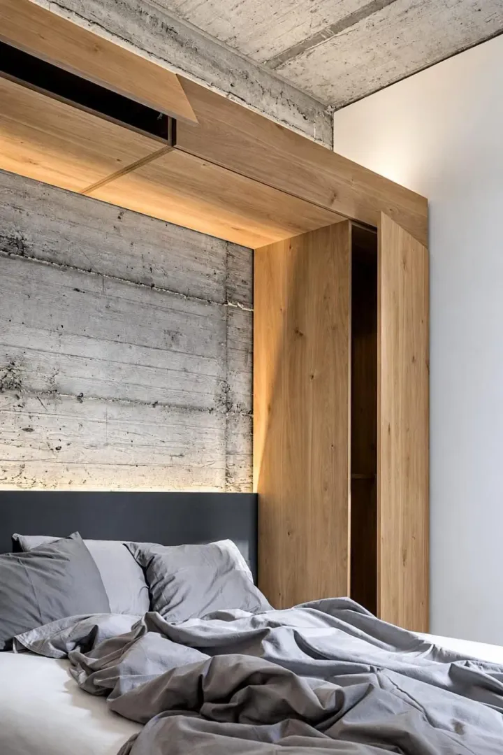 Modern bedroom with wooden elements and an exposed concrete wall.