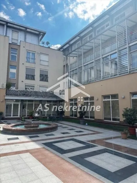 Unutrašnje dvorište zgrade sa popločanim platoom i fontanom.