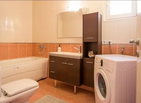 Bathroom equipped with a bathtub, vanity with sink, toilet, and washing machine. - image 6