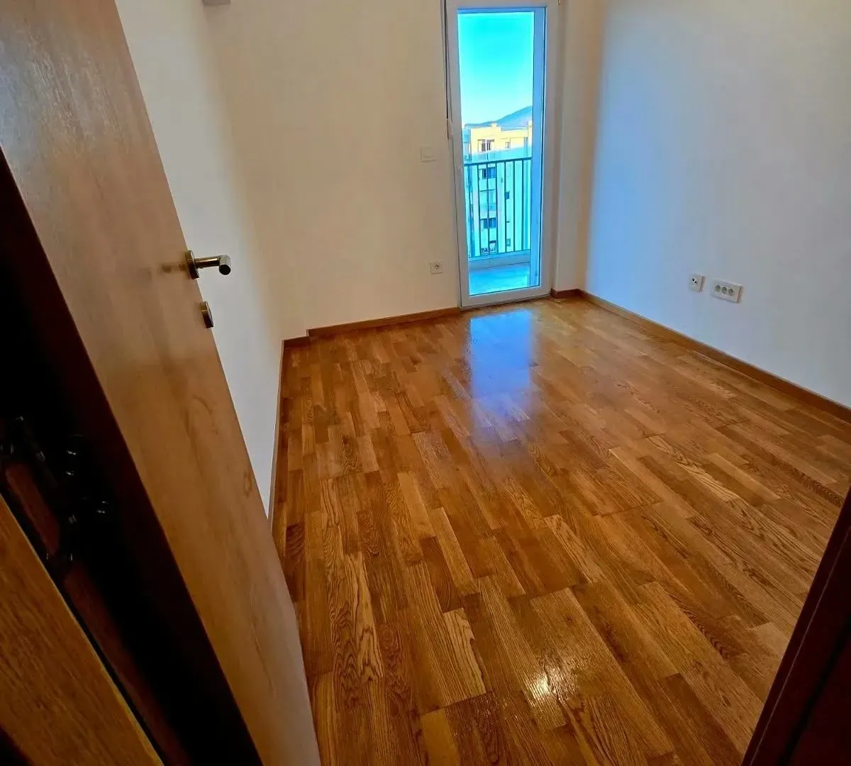 Prazna soba sa parketom i izlazom na terasu.