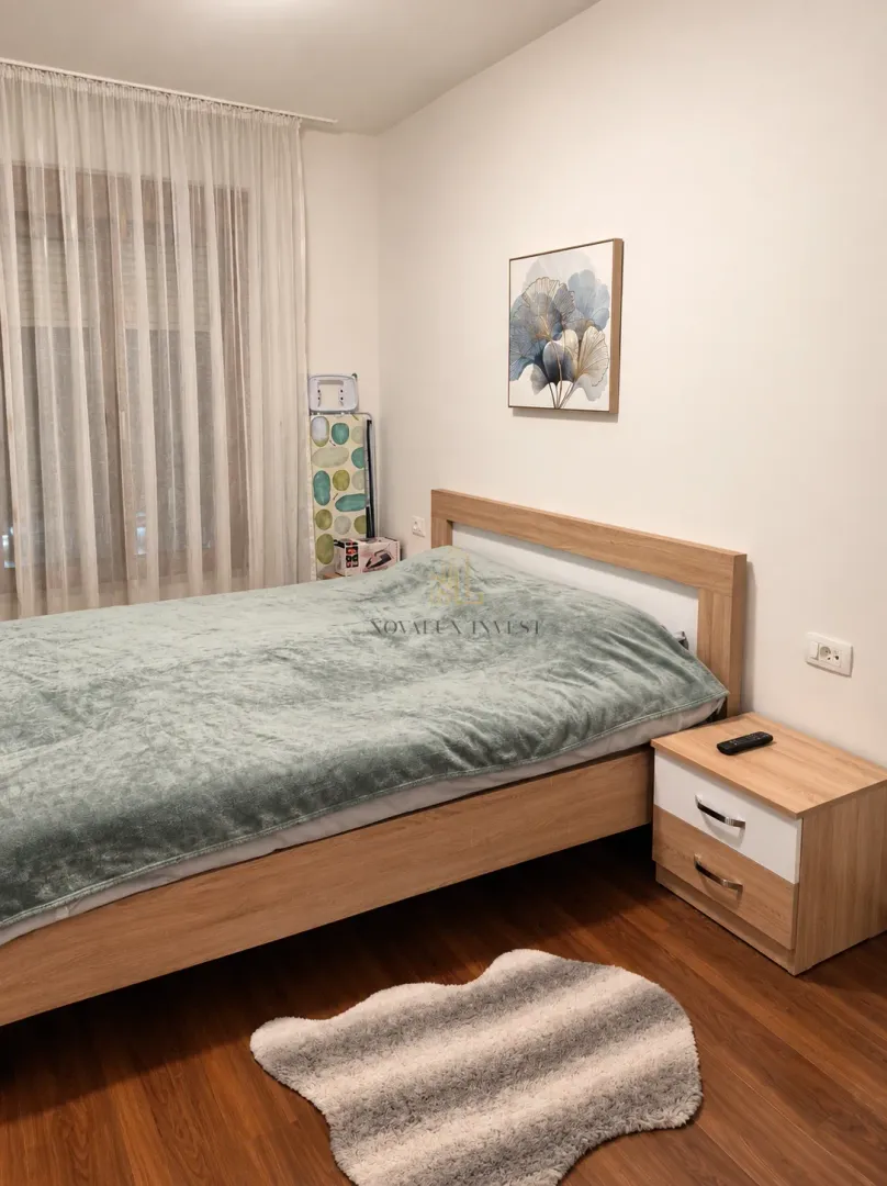 Spavaća soba sa bračnim krevetom, noćnim ormarićem i prozorom sa zavesama.