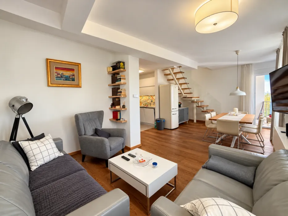 Spacious living room with sofa set, dining area, and stairs in the background.