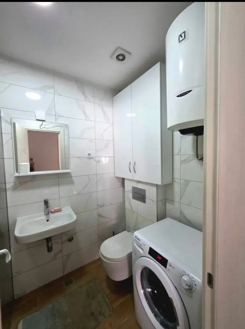 Small bathroom with white tiles, sink, toilet, water heater, and washing machine.