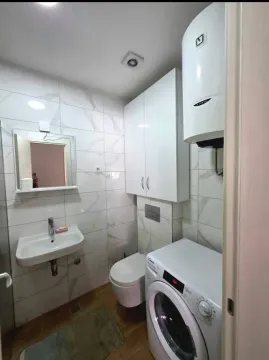 Small bathroom with white tiles, sink, toilet, water heater, and washing machine. - image 8