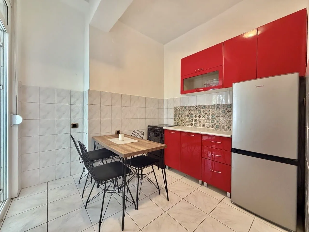 Kitchen with red cabinets, a refrigerator, and a small dining table with chairs.