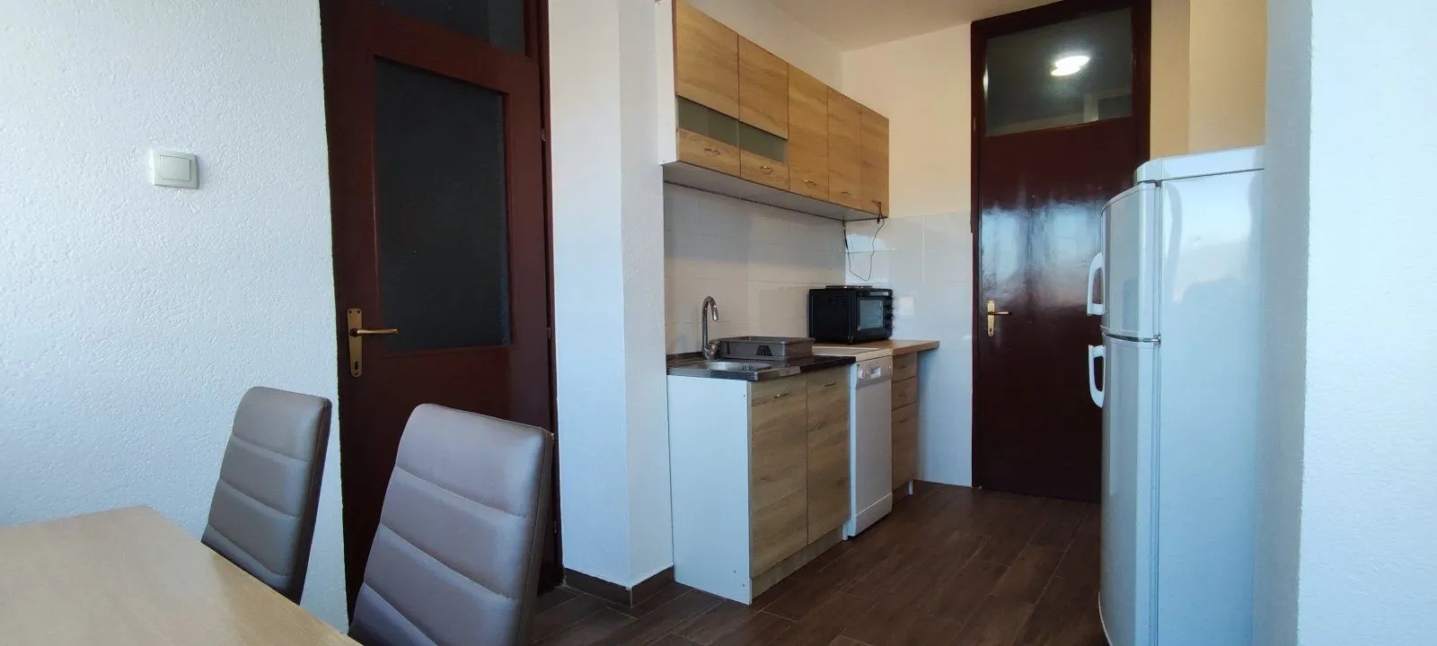 A simple kitchen with wooden cabinets and a refrigerator.