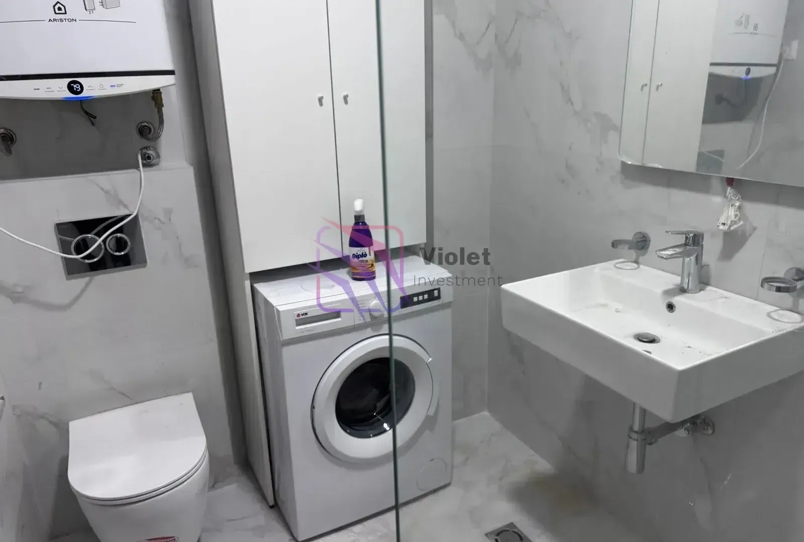 Modernly equipped bathroom with a washbasin, toilet, washing machine, and cabinet.