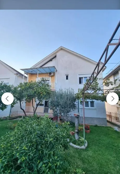 Dvorište i fasada dvospratne kuće sa zelenilom.