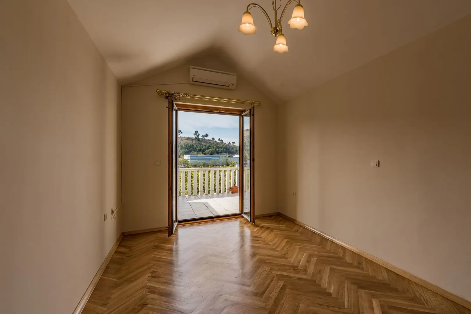 An empty room with parquet flooring and open doors leading to a balcony.