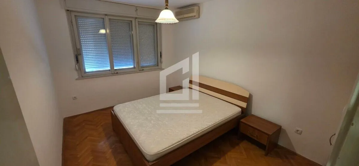 Spavaća soba sa bračnim krevetom, noćnim stočićima i prozorom sa roletnama.