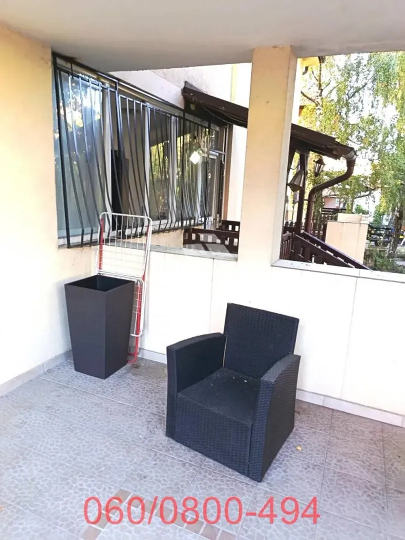 Covered terrace with a black armchair and a clothes drying rack.
