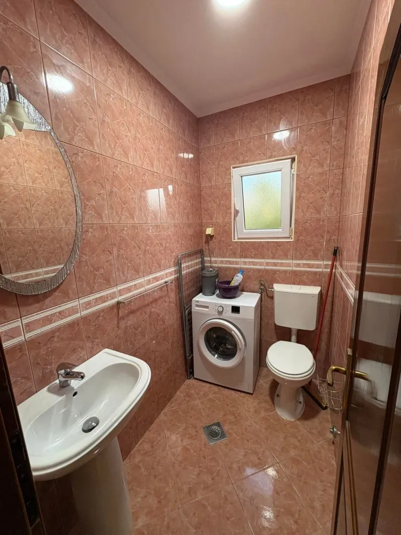 Smaller tiled bathroom with a sink, washing machine, and toilet.
