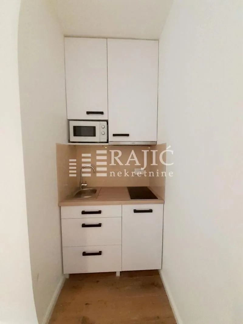 Small white kitchen with built-in oven, microwave and sink.