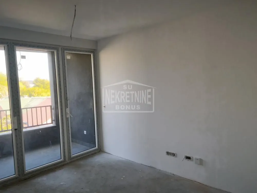 Prazna neopremljena prostorija u izgradnji sa balkonskim vratima i izlazom na terasu.