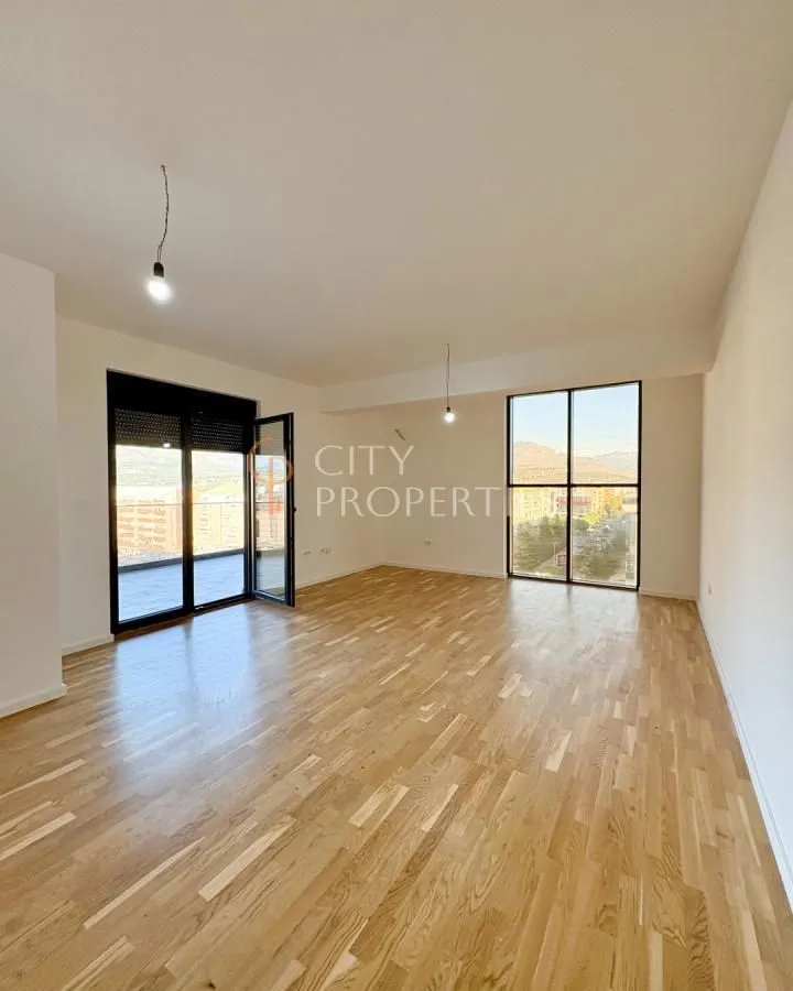 Empty room with wooden parquet flooring and large windows offering a city view.