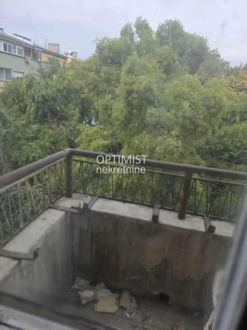 Pogled sa balkona na zelene krošnje i okolne zgrade.