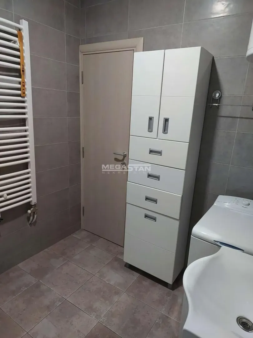 Kupatilo sa pločicama, belim ormarićem i radijatorom.