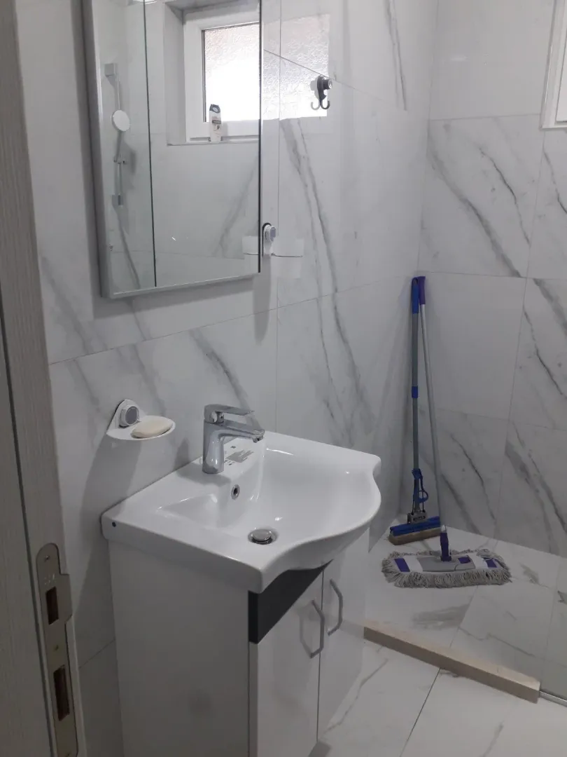 Kupatilo sa bijelim lavaboom, ogledalom i pločicama sa dezenom mermera.