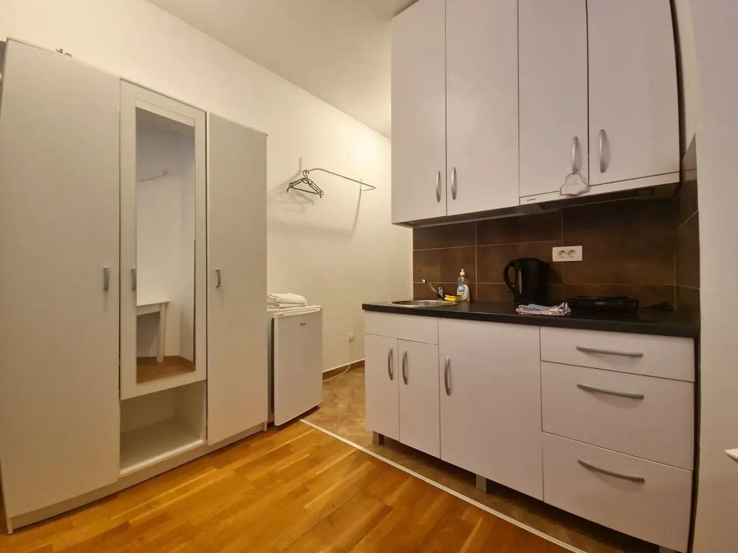 Small kitchen with white cabinets and a built-in wardrobe in the continuation of the room.