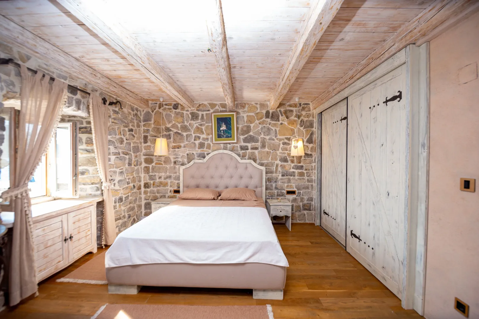 Rustic bedroom with a stone wall and wooden ceiling beams.