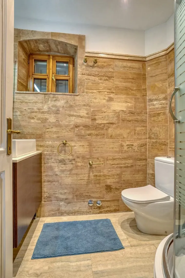 Manje kupatilo obloženo keramičkim pločicama u tonovima kamena sa sanitarijama.