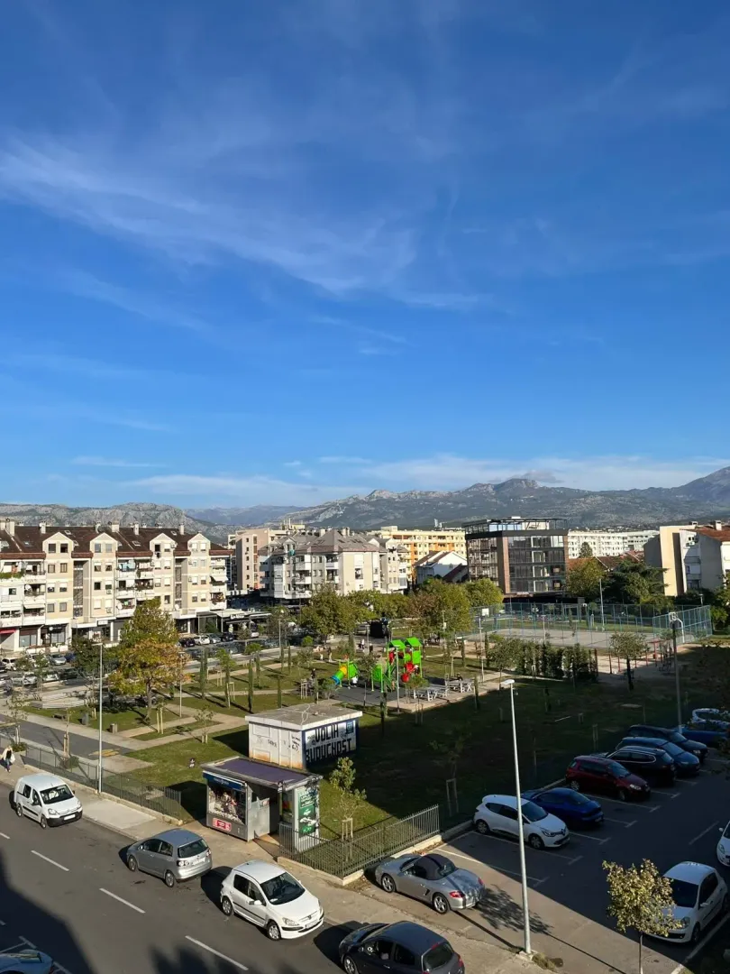 Pogled sa terase na gradski park i okolne zgrade sa planinama u pozadini.