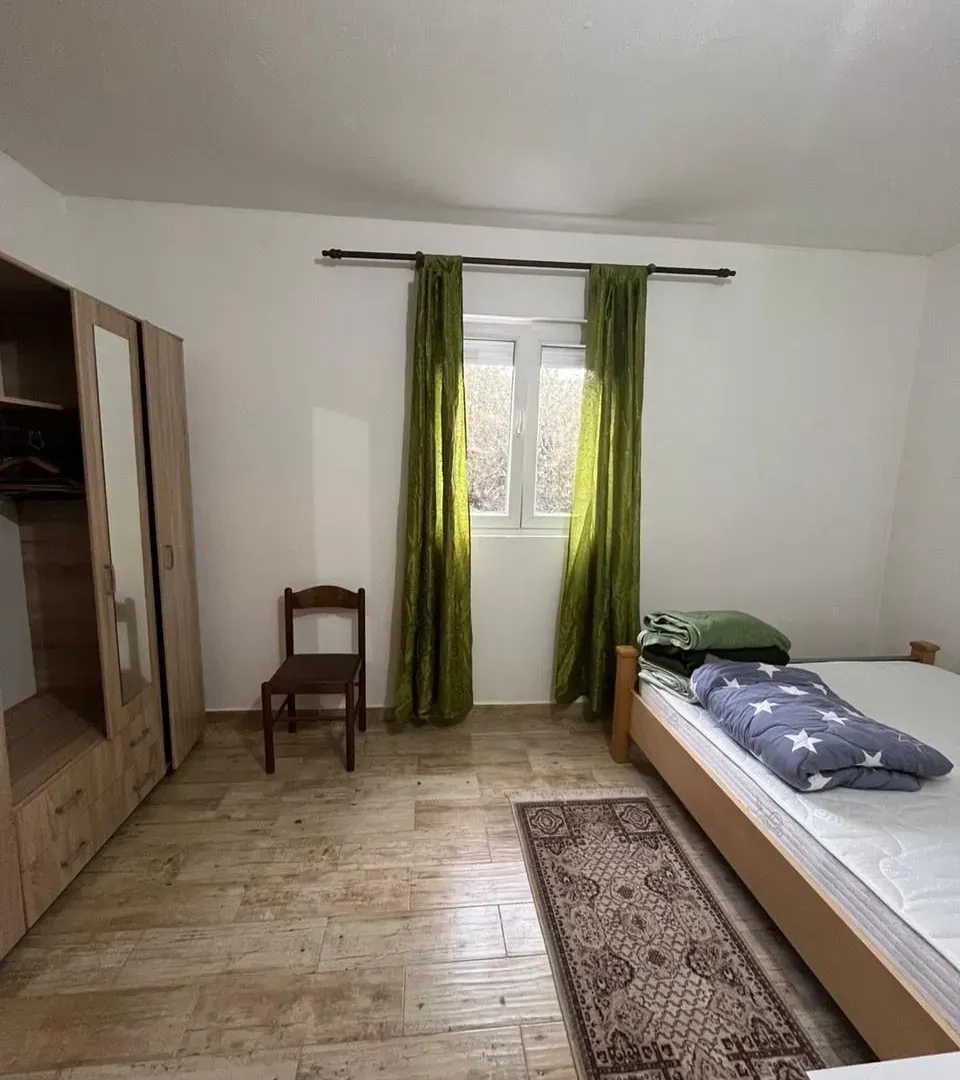 Spavaća soba sa krevetom, ormarom, stolicom i prozorom sa zelenim zavjesama.
