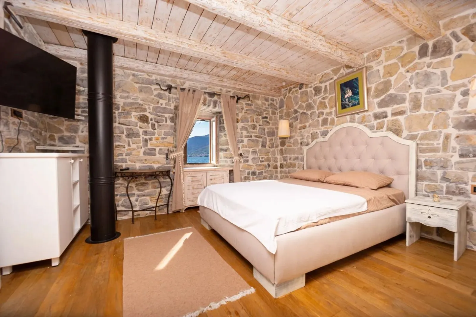 Furnished bedroom with stone walls and a wooden ceiling.