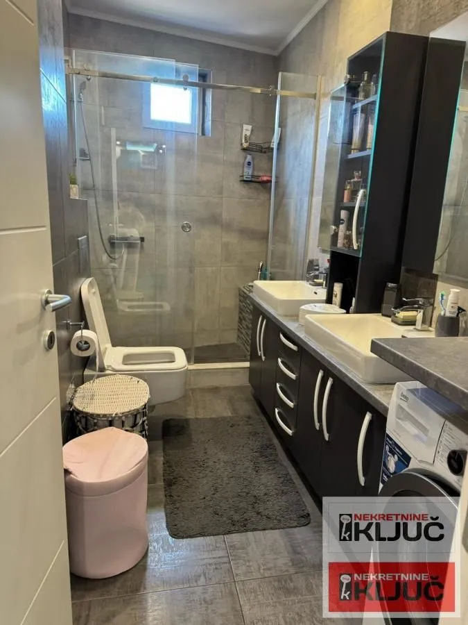 Moderno kupatilo sa tuš kabinom, dva umivaonika i WC šoljom.