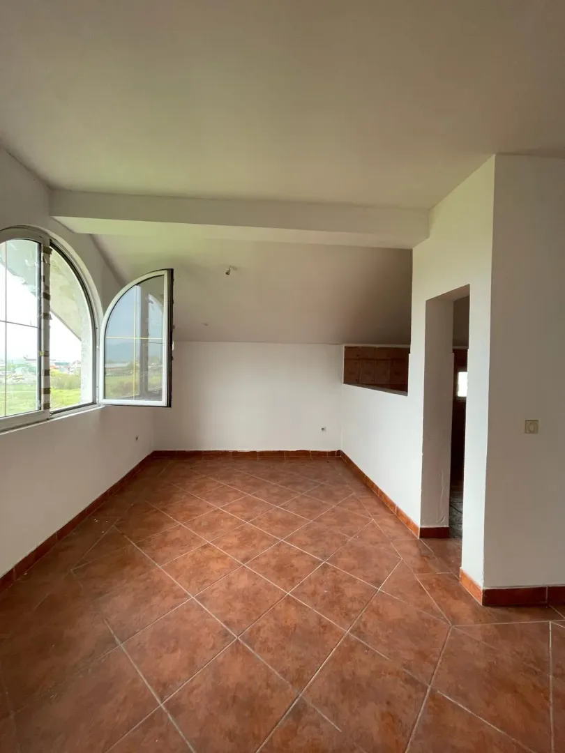 Prazna prostorija sa terakot pločicama i lučnim prozorom.