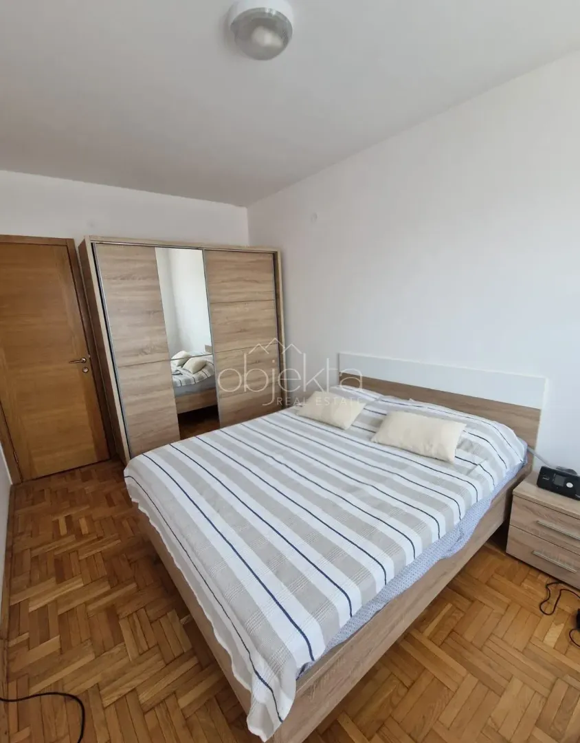 Furnished bedroom with a double bed, wardrobe, and wooden parquet flooring.