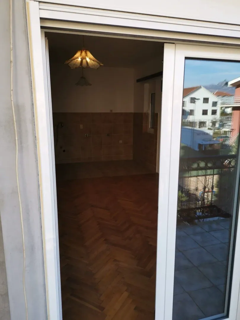 Pogled kroz otvorena balkonska vrata na praznu prostoriju sa parketom.