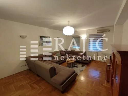Spacious living room with a sectional sofa and wooden parquet flooring.