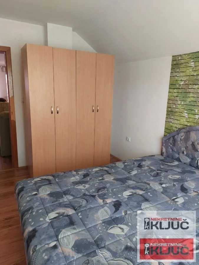 Nameštena spavaća soba sa bračnim krevetom i drvenim ormanom.