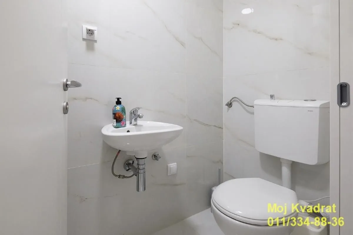 Smaller bathroom with a washbasin and toilet, lined with light marble tiles.