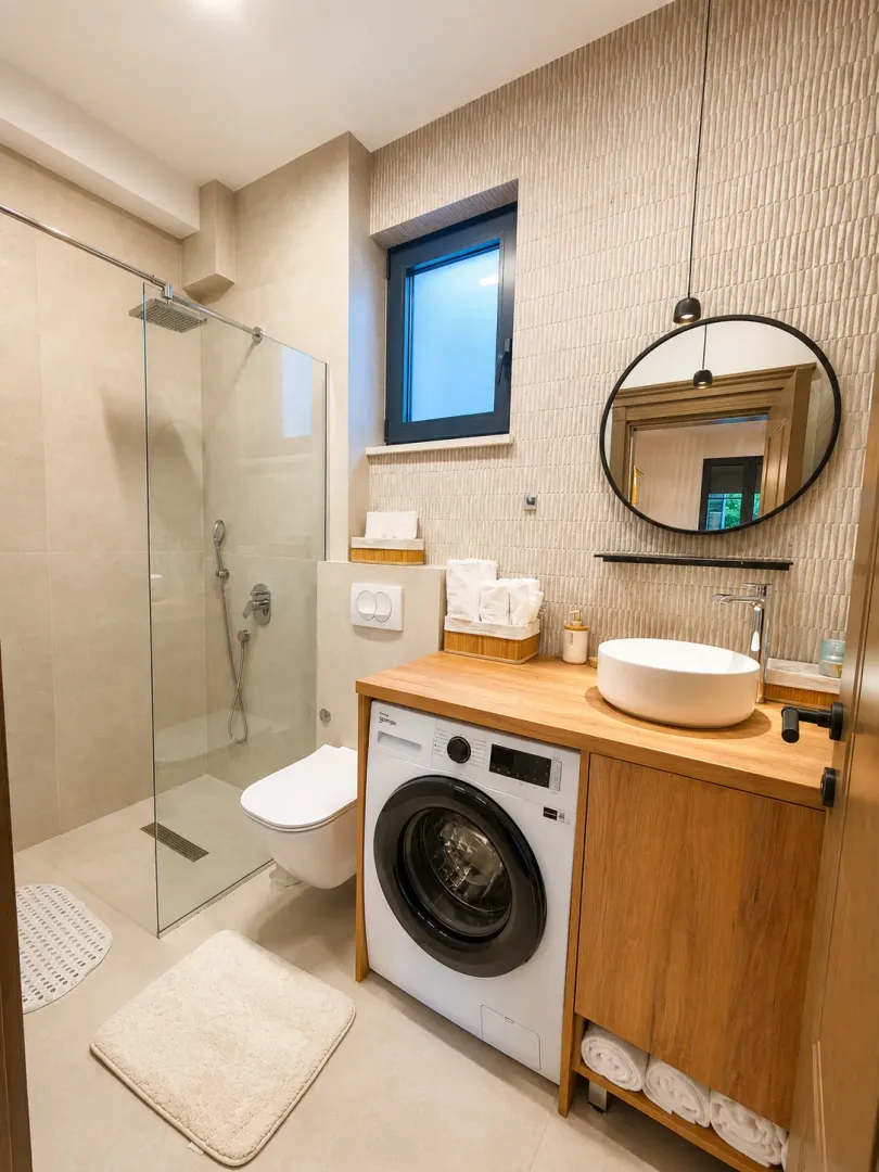 Modernly equipped bathroom with a walk-in shower, washbasin, and washing machine.