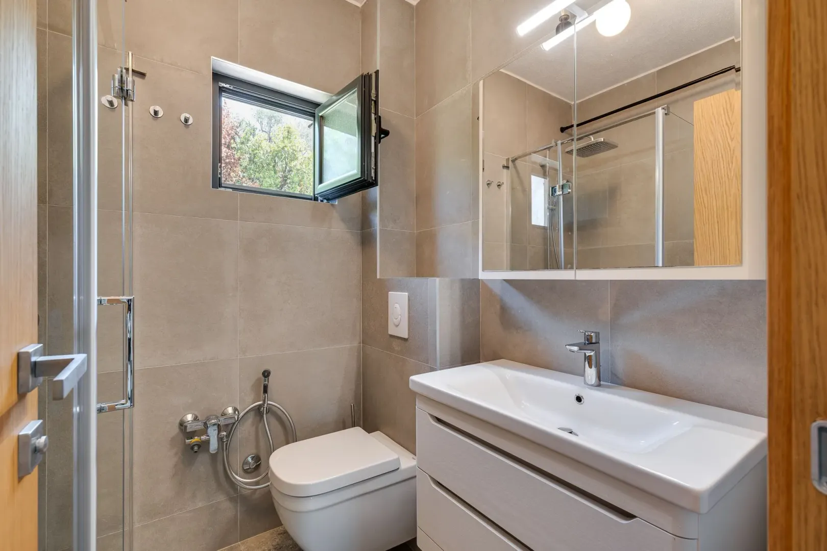 Savremeno opremljeno kupatilo sa tuš kabinom, umivaonikom i WC šoljom.