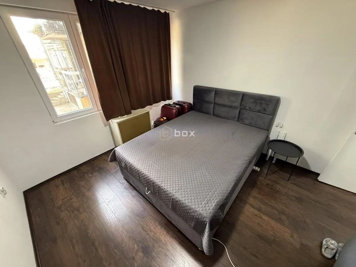 Nameštena spavaća soba sa bračnim krevetom, tamnim laminatom i prozorom.