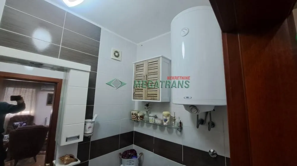 View of the bathroom with tiles, water heater, and a cabinet.
