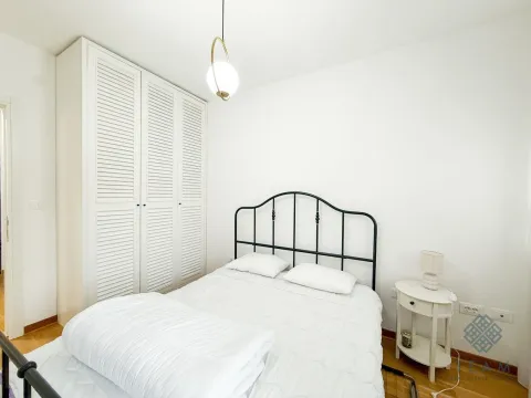 Svjetla spavaća soba sa bračnim krevetom, bijelim ormarom i noćnim stočićem. - image 6
