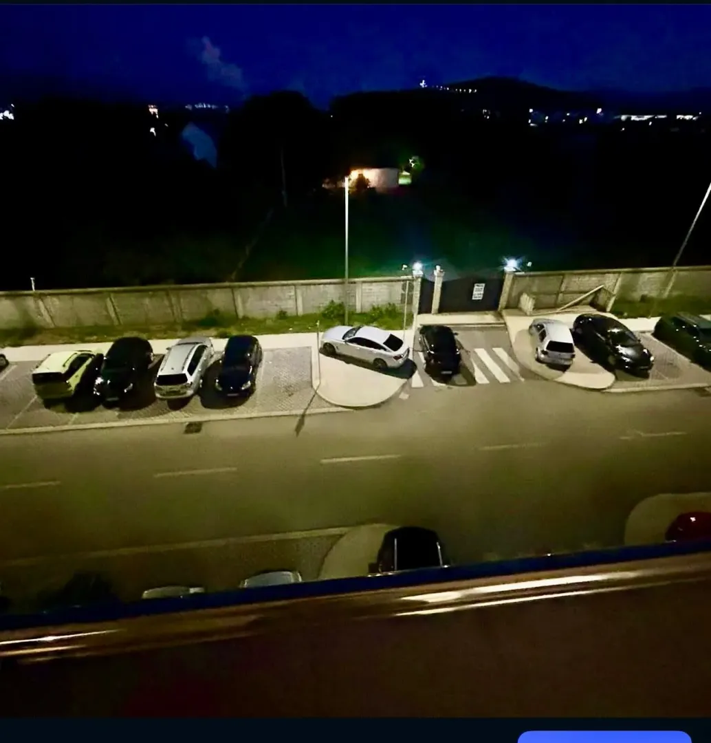 Pogled sa terase na parking prostor ispred zgrade noću.