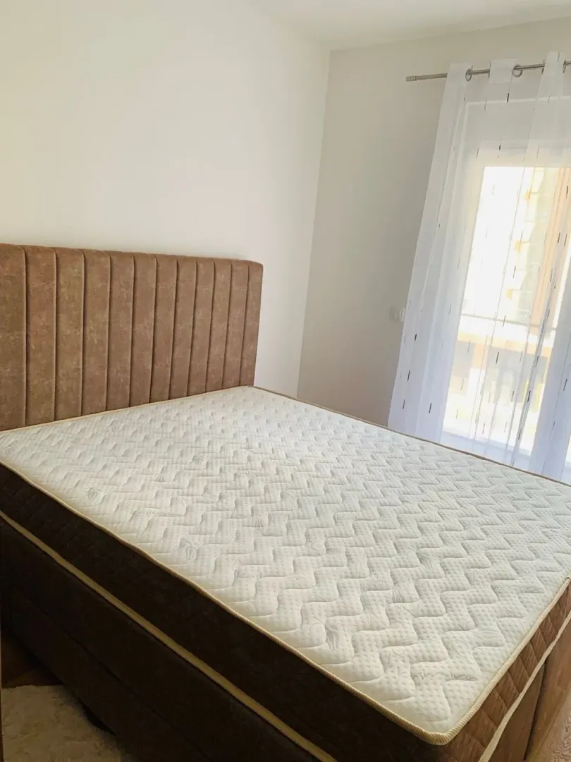 Bright bedroom with a double bed and a window covered with a white curtain.